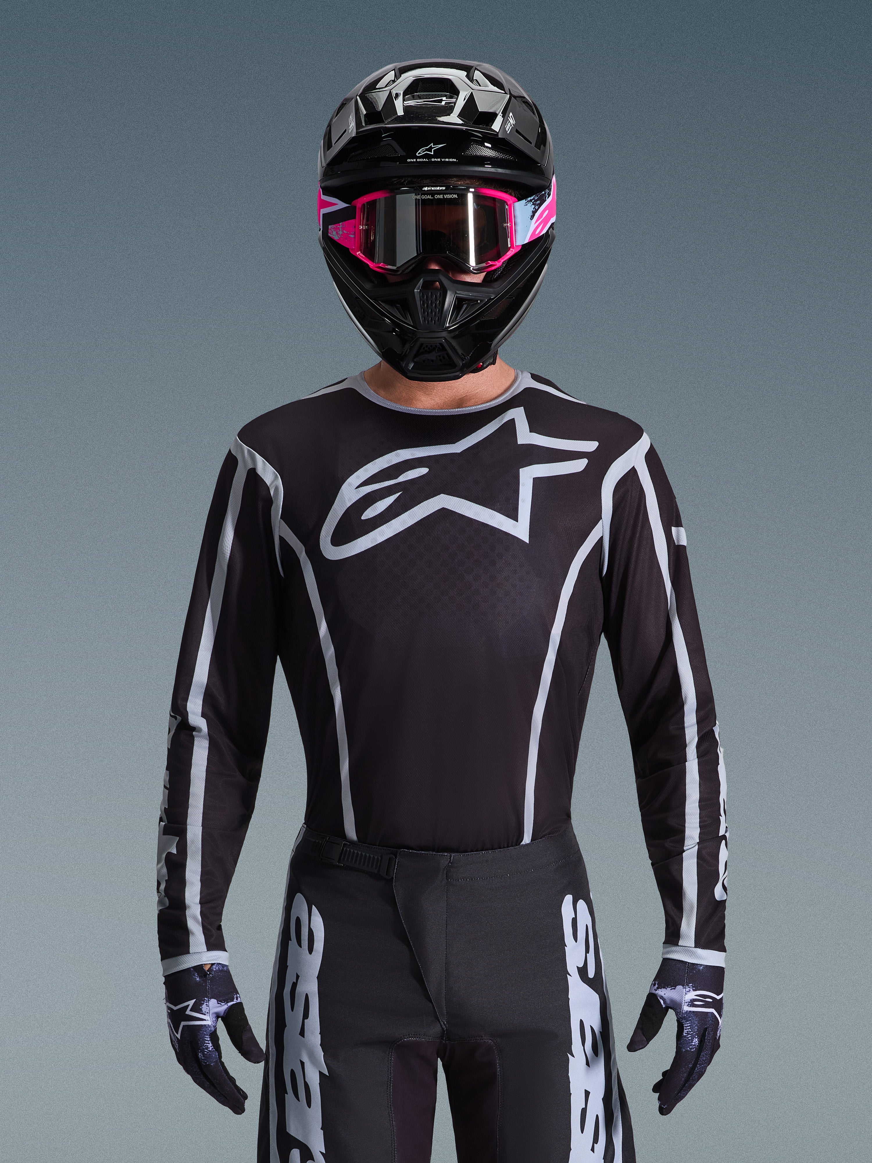 Zestaw Alpinestars 2026 Fluid Apex, koszulka i spodnie motocrossowe w kolorze czarno-białym, duże logo na klatce piersiowej i geometryczne wzory linii, czarny kask i różowe gogle, profesjonalna odzież do wyścigów motocrossowych.