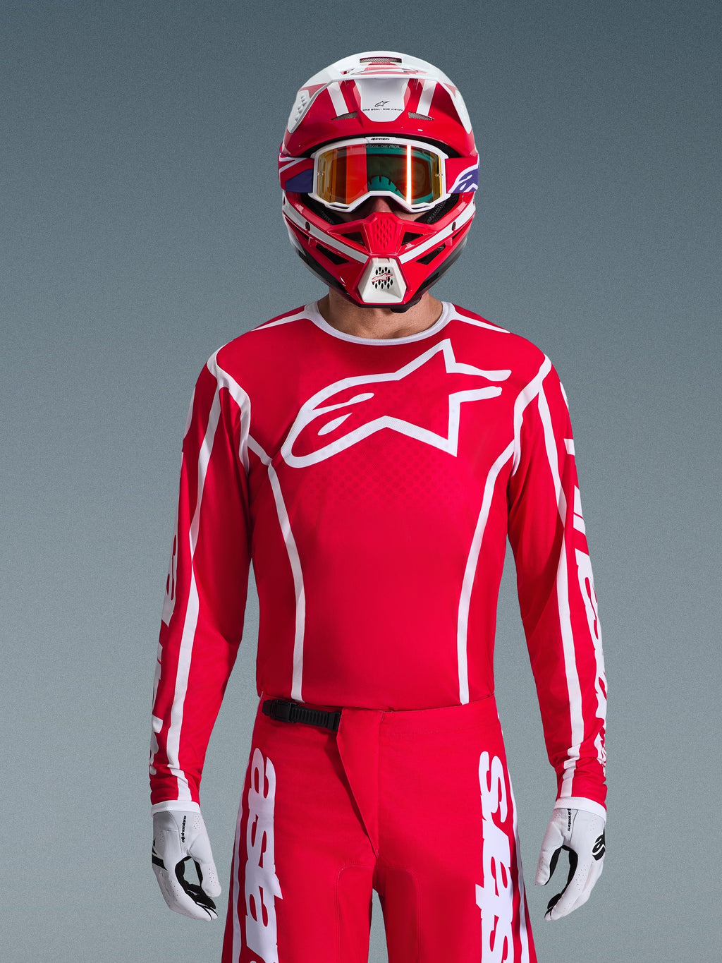 Alpinestars 2026 Fluid Apex Jersey, koszulka motocrossowa, czerwono-biała, noszona przez motocyklistę w dopasowanym czerwono-białym kasku i pomarańczowych goglach, z wyraźnym białym logo na piersi, sportowy krój, element spójnego zestawu odzieży wyścigowej off-road