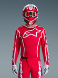 Alpinestars 2026 Fluid Apex Jersey, koszulka motocrossowa, czerwono-biała, noszona przez motocyklistę w dopasowanym czerwono-białym kasku i pomarańczowych goglach, z wyraźnym białym logo na piersi, sportowy krój, element spójnego zestawu odzieży wyścigowej off-road