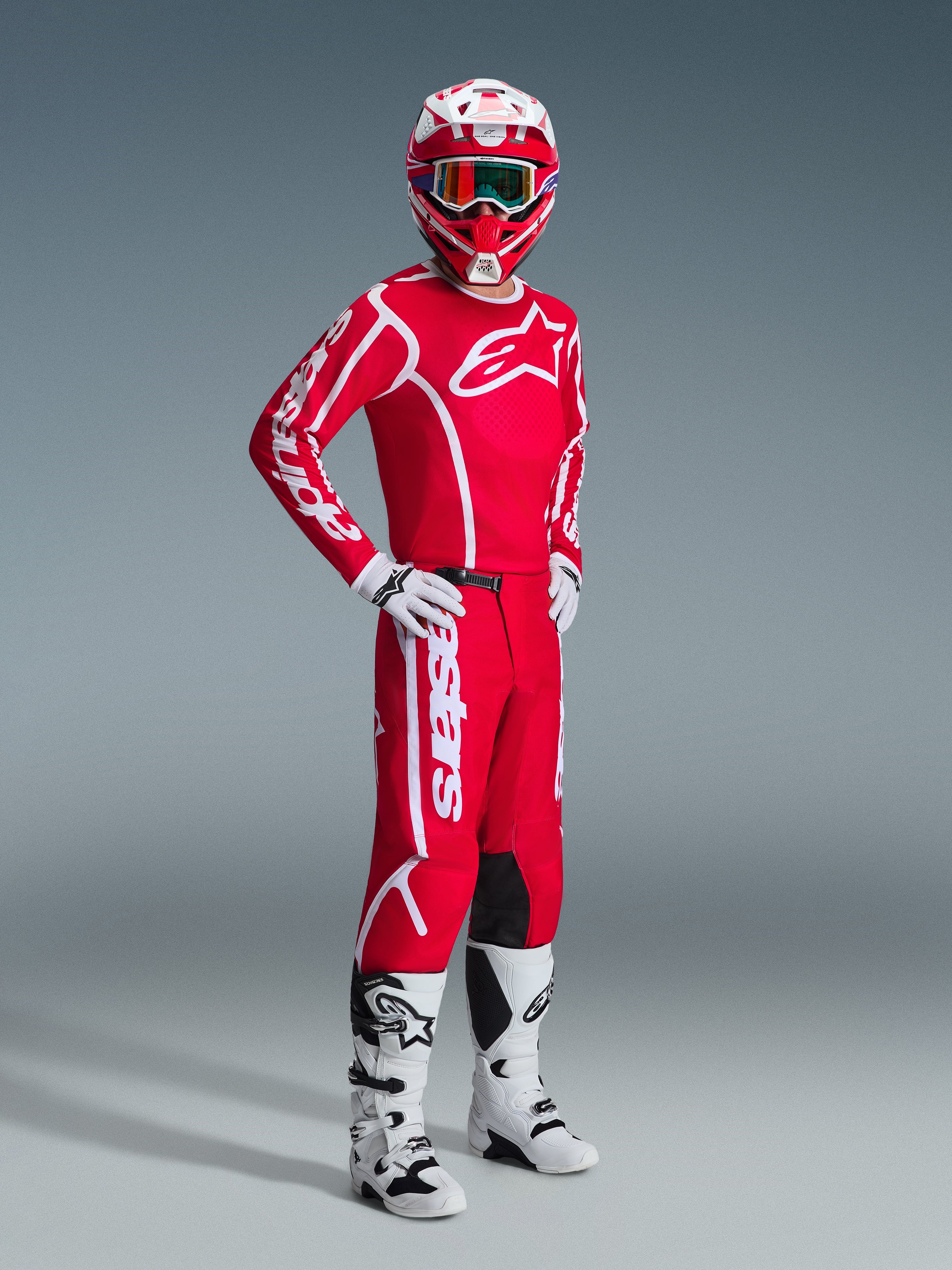 Motocyklista w zestawie Alpinestars 2026 Fluid Apex, czerwona koszulka z dużym białym logo, czerwone spodnie z białymi akcentami, biało-czerwony kask, białe buty i rękawice motocrossowe, skoordynowany strój do wyścigów off-road