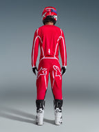 Widok z tyłu motocyklisty motocrossowego w zestawie Alpinestars 2026 Fluid Apex, jaskrawoczerwona koszulka i spodnie z białymi pasami i logo, biało-czarne buty i czerwony kask, profesjonalny strój do wyścigów terenowych