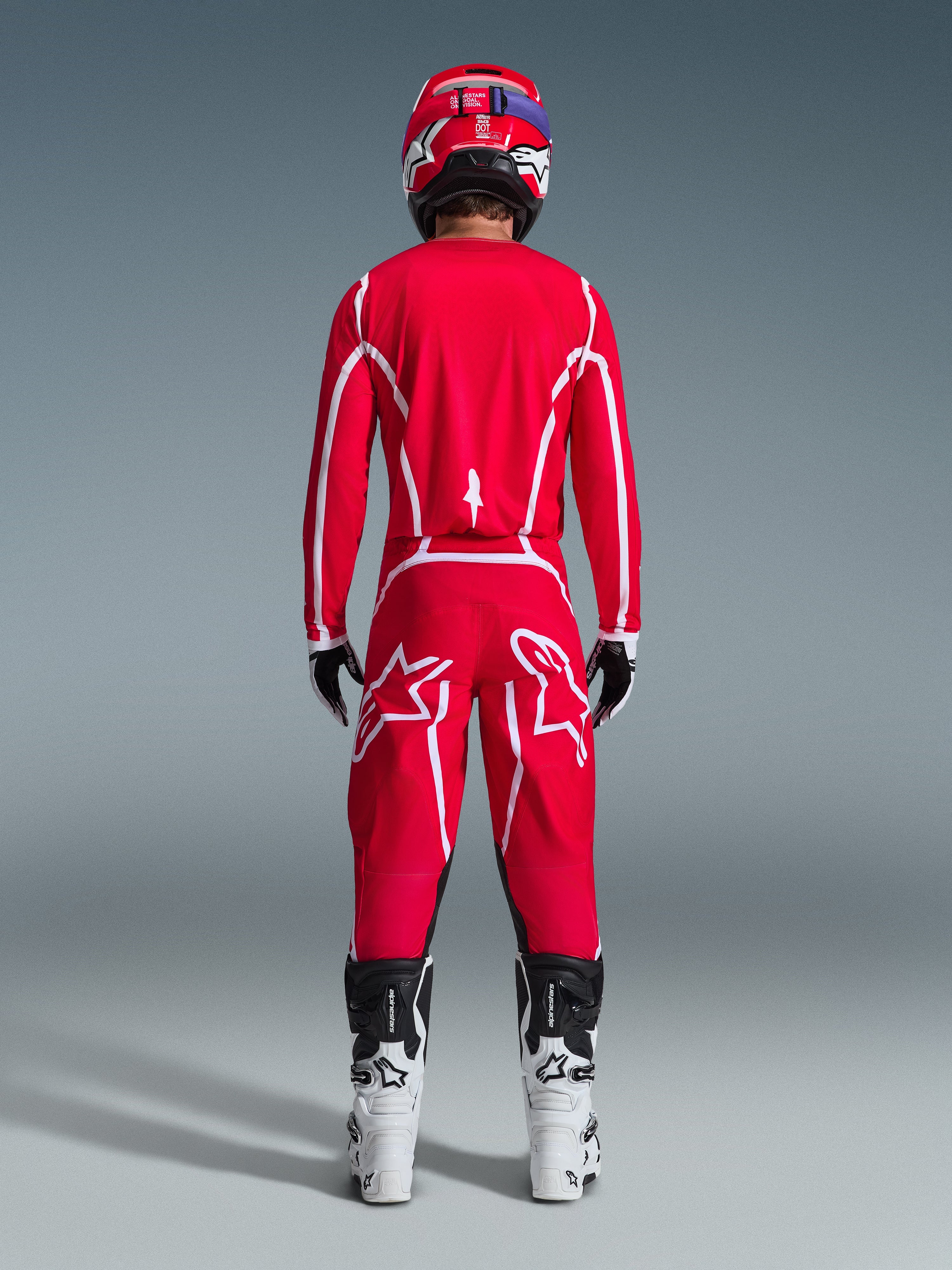 Widok z tyłu motocyklisty motocrossowego w zestawie Alpinestars 2026 Fluid Apex, jaskrawoczerwona koszulka i spodnie z białymi pasami i logo, biało-czarne buty i czerwony kask, profesjonalny strój do wyścigów terenowych