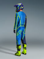 Zestaw Alpinestars 2026 Fluid Apex, motocyklista motocrossowy widoczny od tyłu w niebiesko-neonowożółtym stroju, niebieska koszulka i spodnie z neonowożółtymi logotypami, neonowożółte buty, fioletowo-niebieski kask, dopasowana odzież do wyścigów off-road.