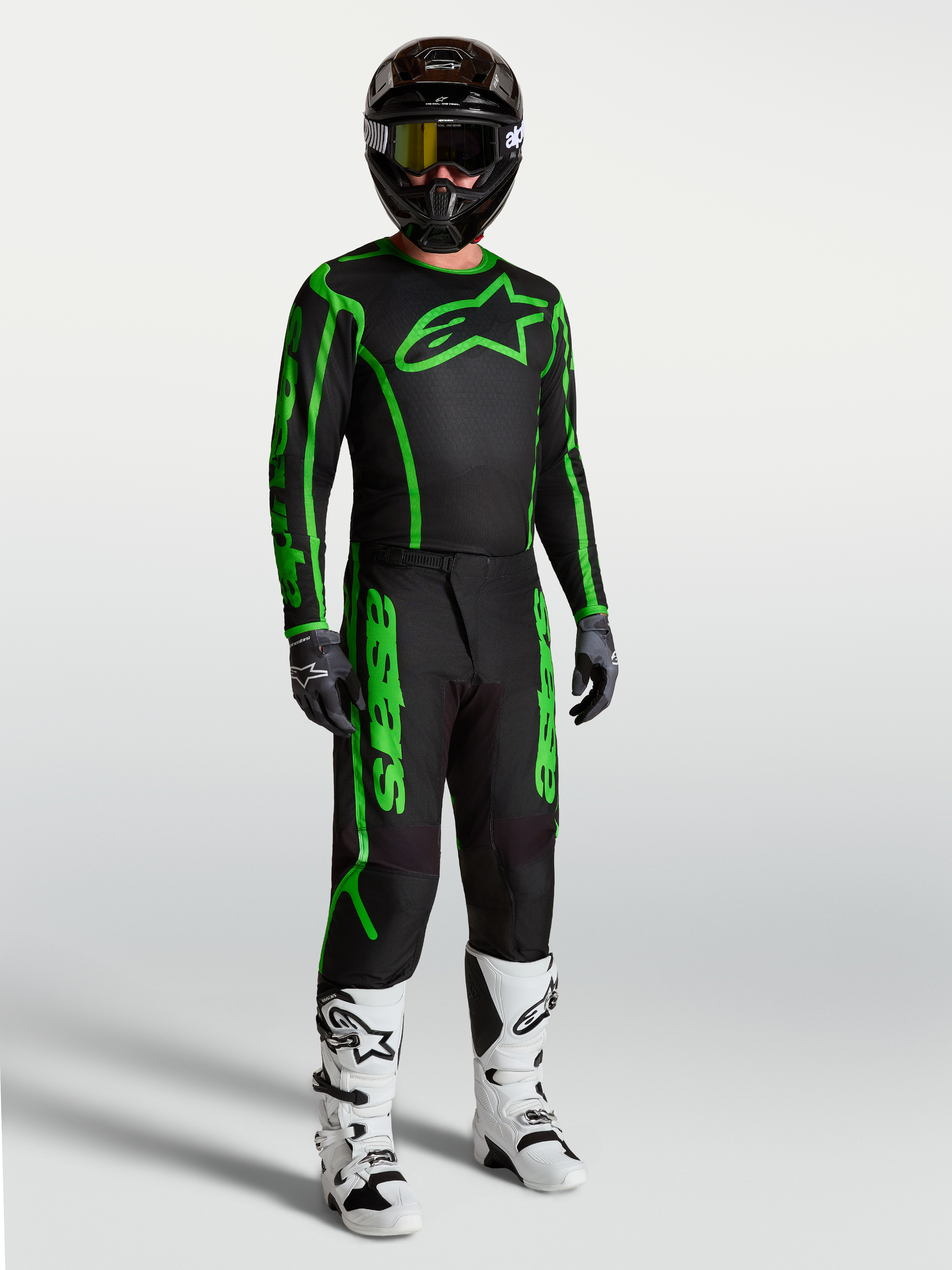 Alpinestars Spodnie Fluid Apex V2, męskie spodnie motocrossowe, czarne i zielone fluo, wytrzymały poliester 600D, ergonomiczny krój, widoczne w pełnym zestawie z białymi butami motocyklowymi.