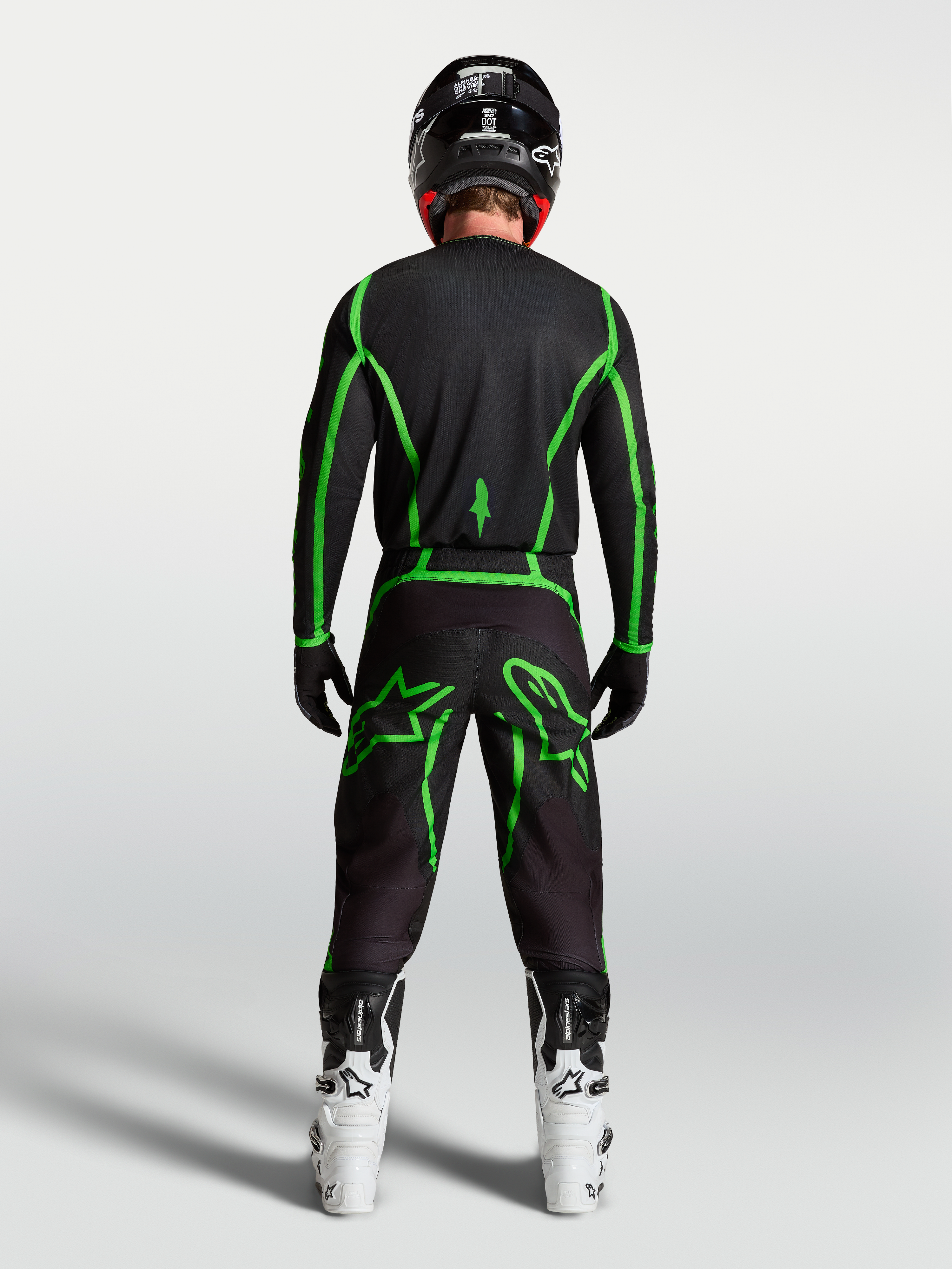 Alpinestars spodnie Fluid Apex V2, czarne i zielone fluo spodnie motocrossowe, widok z tyłu na motocykliście, białe buty
