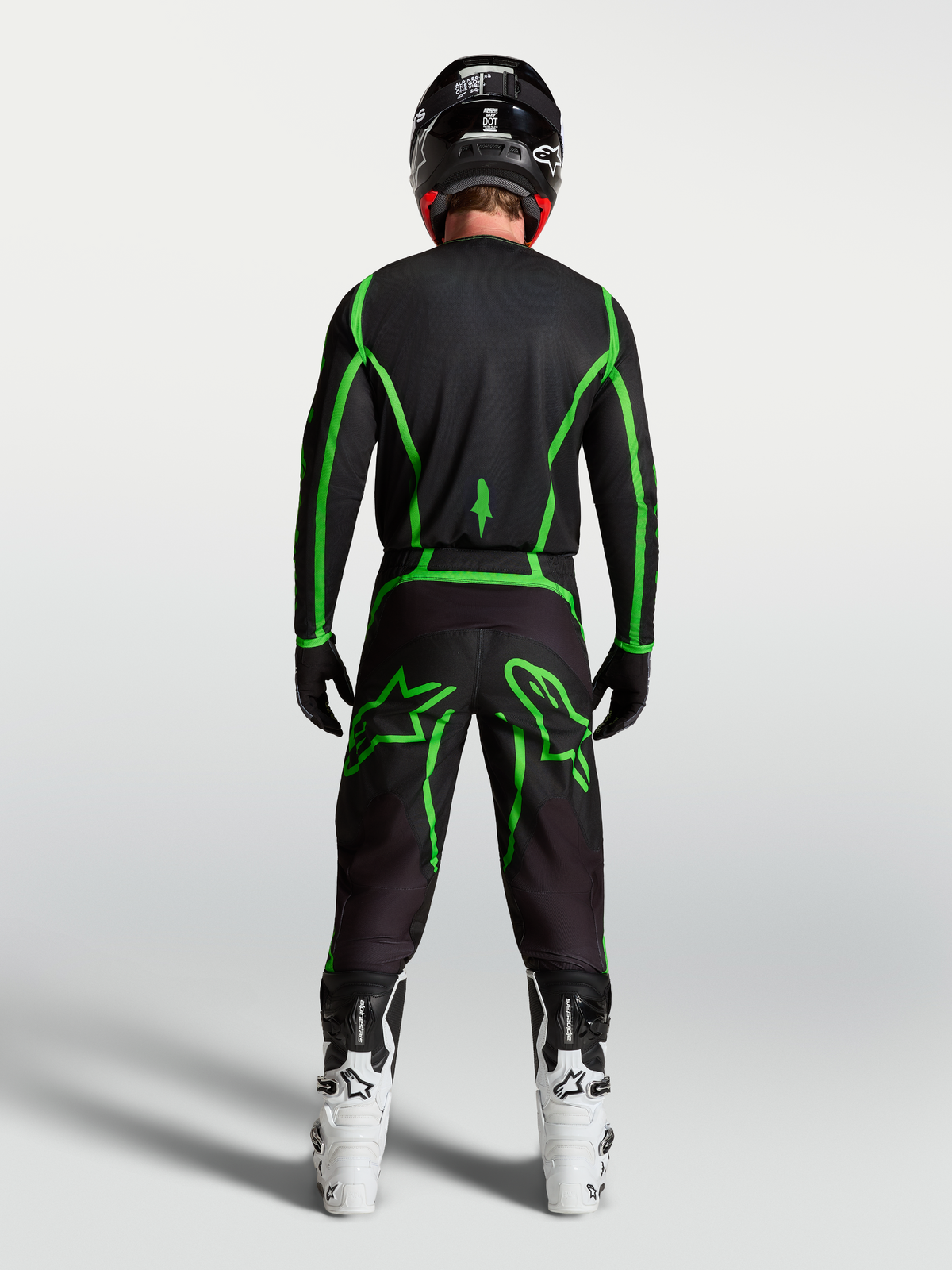 Koszulka Alpinestars Fluid Apex V2, czarno-zielona, widok z tyłu na motocyklistę w białych butach, odzież motocrossowa.