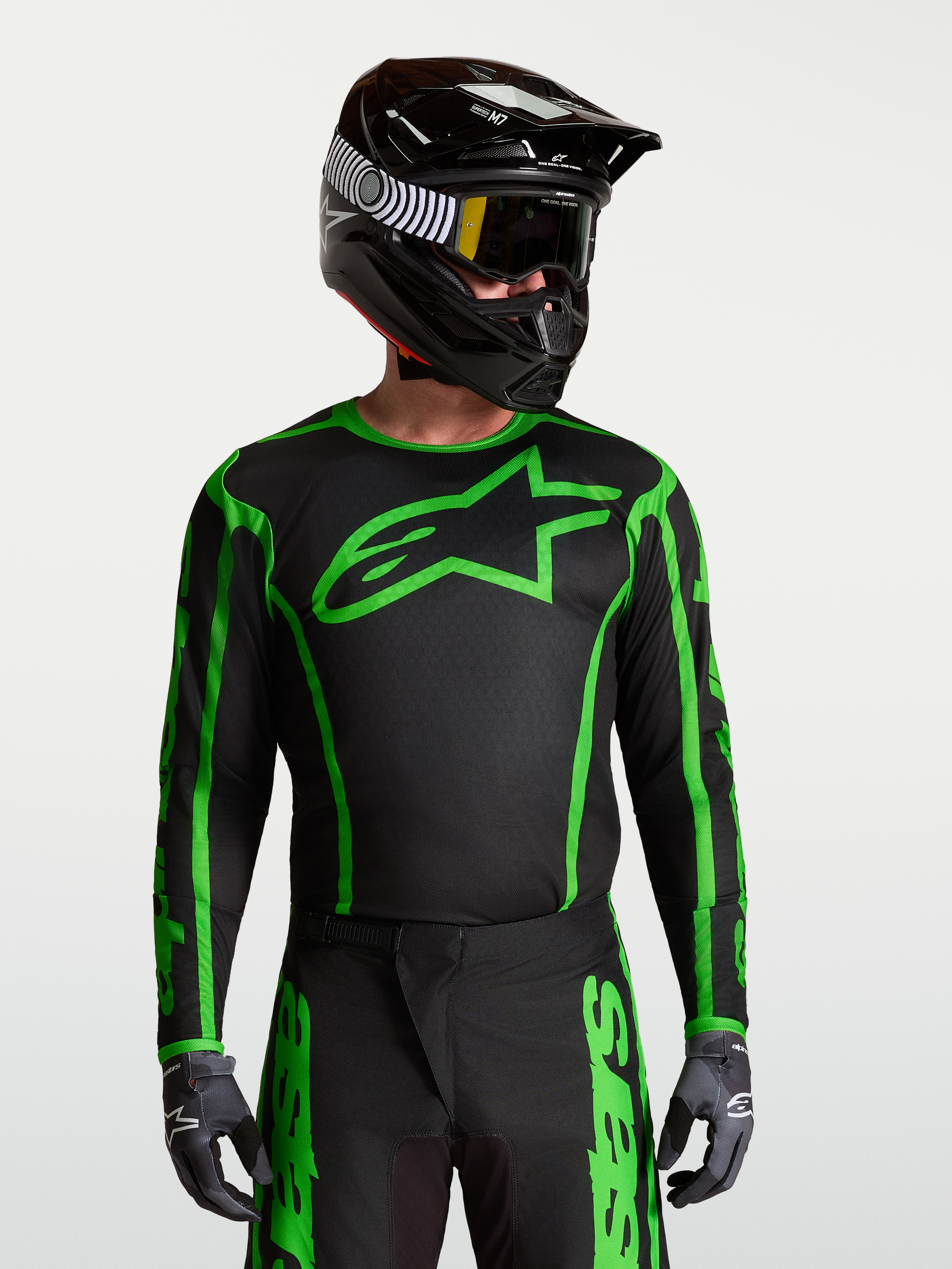 Alpinestars Koszulka Fluid Apex V2, czarno-zielona koszulka motocrossowa na modelu w kasku, odprowadzający wilgoć materiał poliestrowy do jazdy off-road