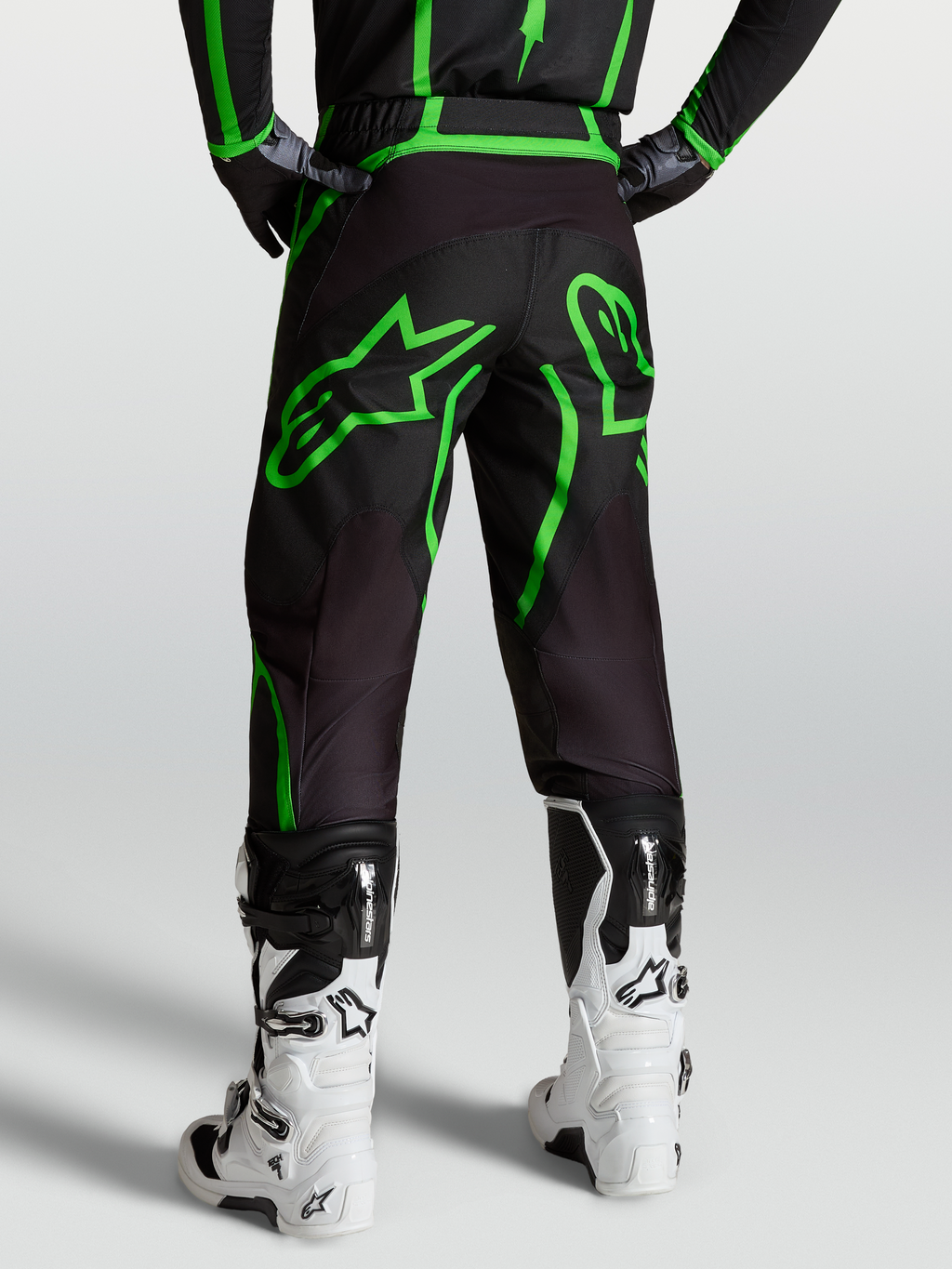 Spodnie Alpinestars Fluid Apex V2, męskie spodnie motocrossowe, czarne i jaskrawozielone, widok od tyłu na modelu w białych butach.