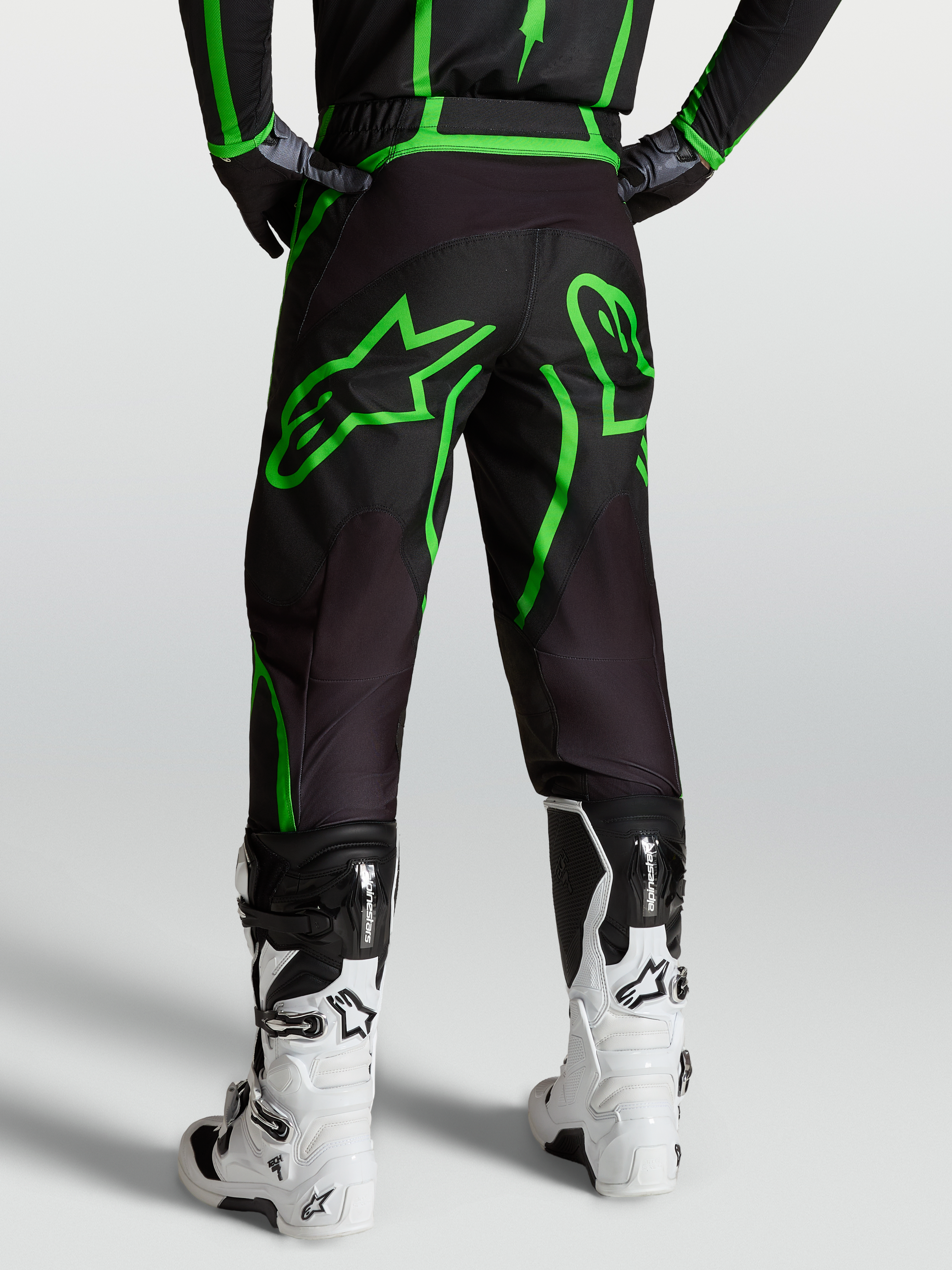 Spodnie Alpinestars Fluid Apex V2, męskie spodnie motocrossowe, czarne i jaskrawozielone, widok od tyłu na modelu w białych butach.