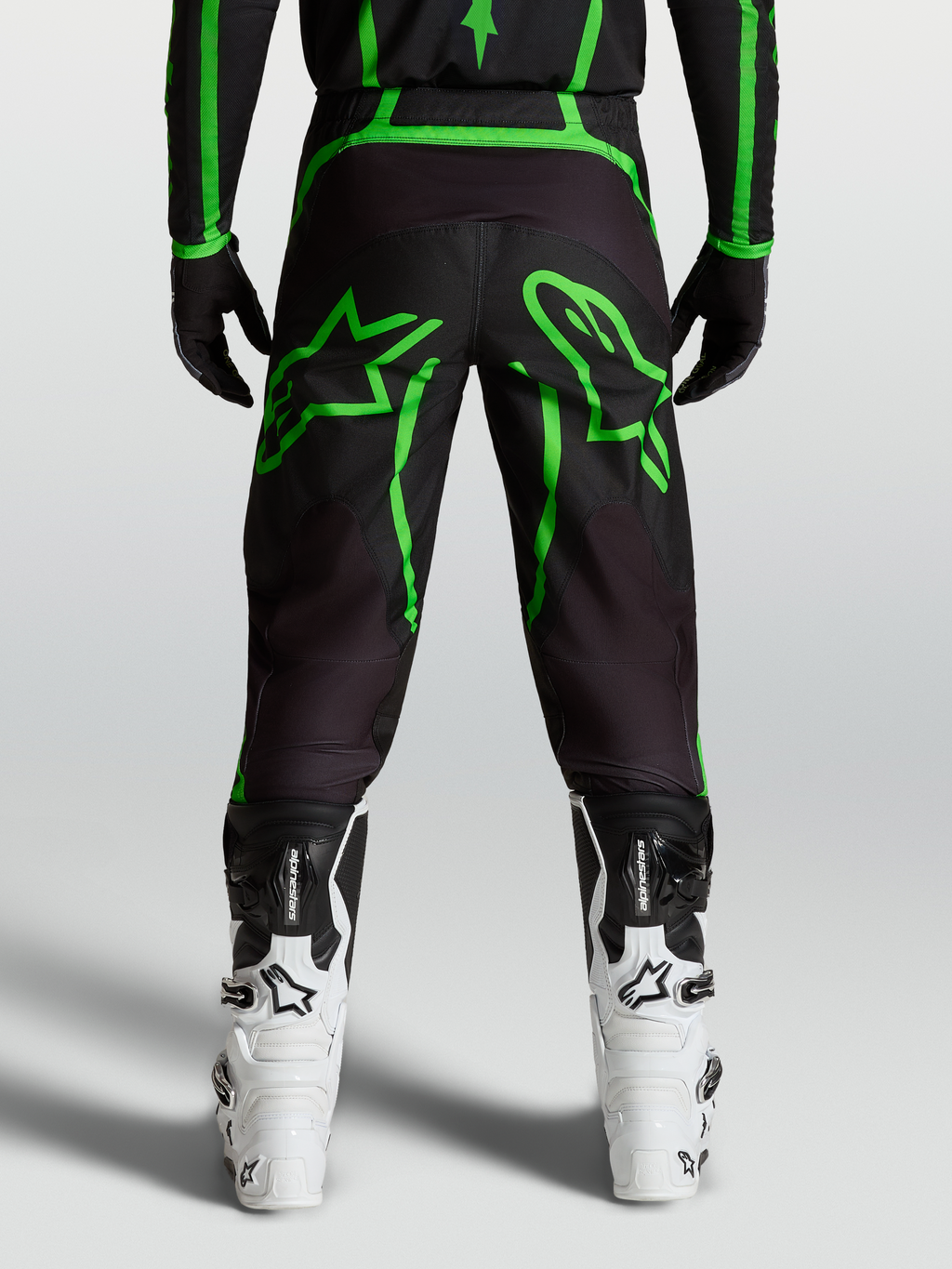 Alpinestars Spodnie Fluid Apex V2, męskie spodnie motocrossowe, czarne i jaskrawozielone z dużą grafiką gwiazdy, widok z tyłu na modelu.