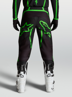 Alpinestars Spodnie Fluid Apex V2, męskie spodnie motocrossowe, czarne i jaskrawozielone z dużą grafiką gwiazdy, widok z tyłu na modelu.