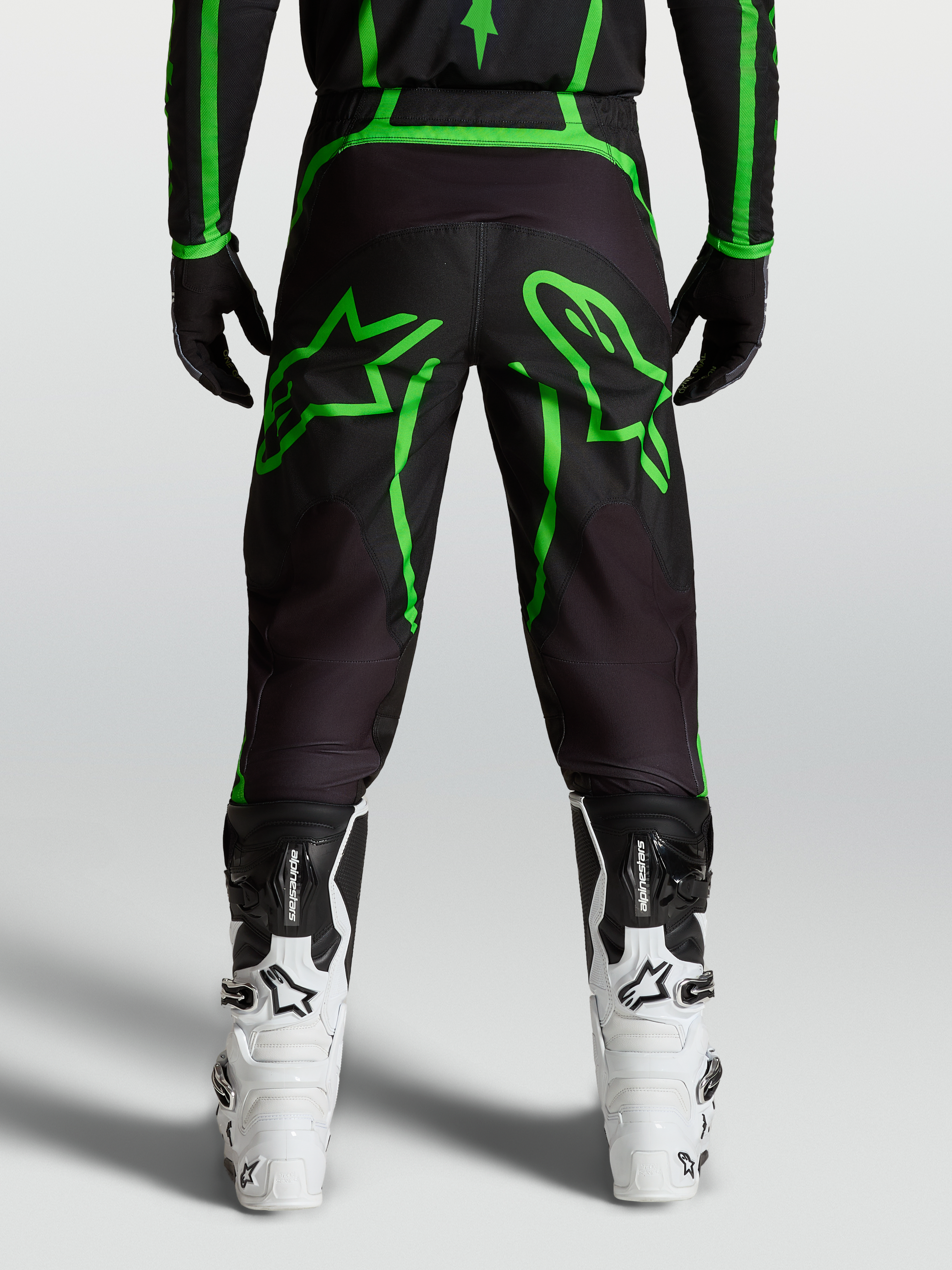 Alpinestars Spodnie Fluid Apex V2, męskie spodnie motocrossowe, czarne i jaskrawozielone z dużą grafiką gwiazdy, widok z tyłu na modelu.