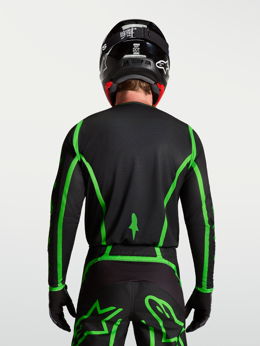 Alpinestars Fluid Apex V2, męska koszulka motocrossowa, czarna i jaskrawozielona, widok z tyłu na modelu ukazujący przedłużony krój pleców.