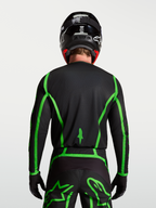 Alpinestars Fluid Apex V2, męska koszulka motocrossowa, czarna i jaskrawozielona, widok z tyłu na modelu ukazujący przedłużony krój pleców.