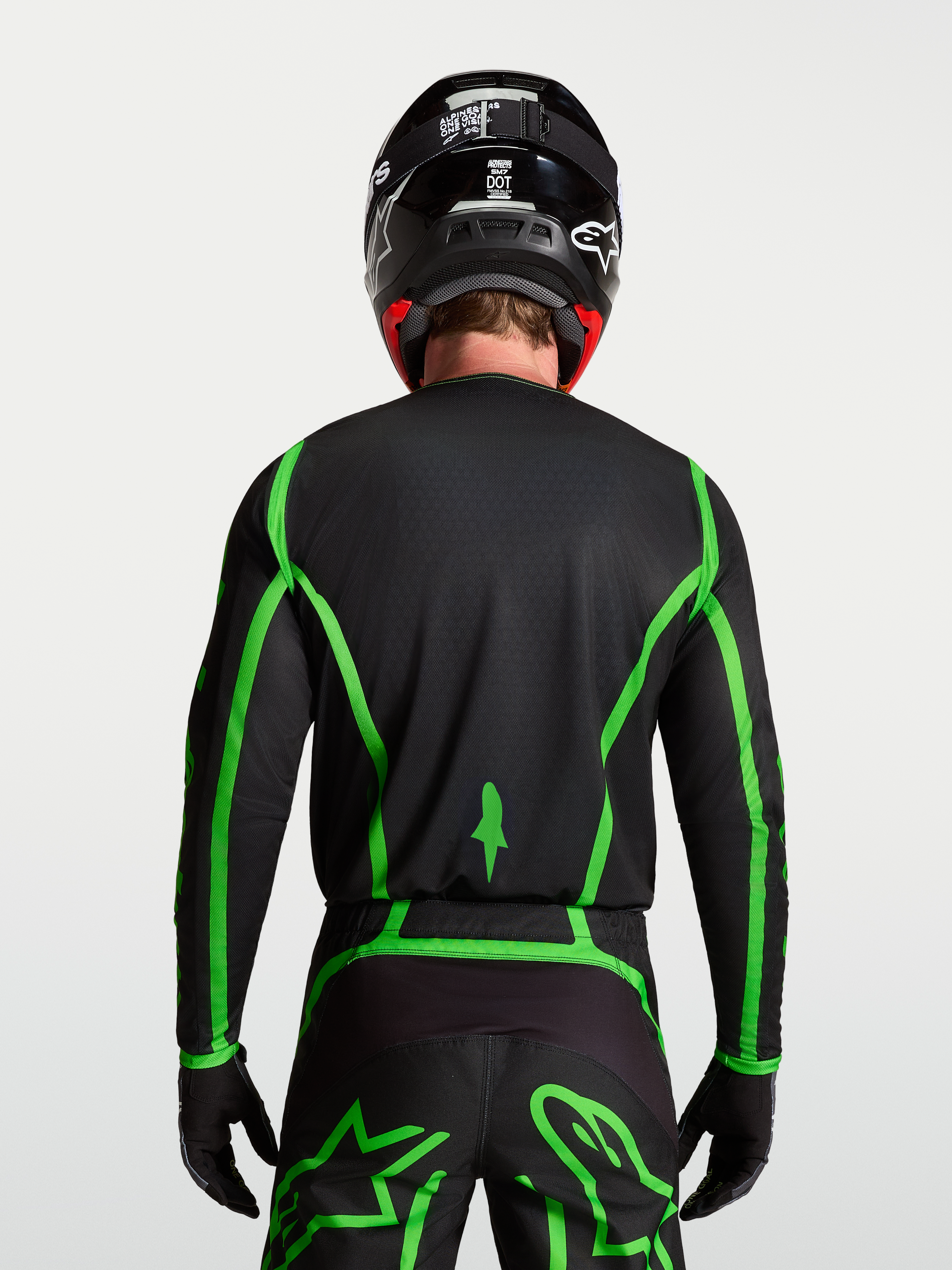 Alpinestars Fluid Apex V2, męska koszulka motocrossowa, czarna i jaskrawozielona, widok z tyłu na modelu ukazujący przedłużony krój pleców.