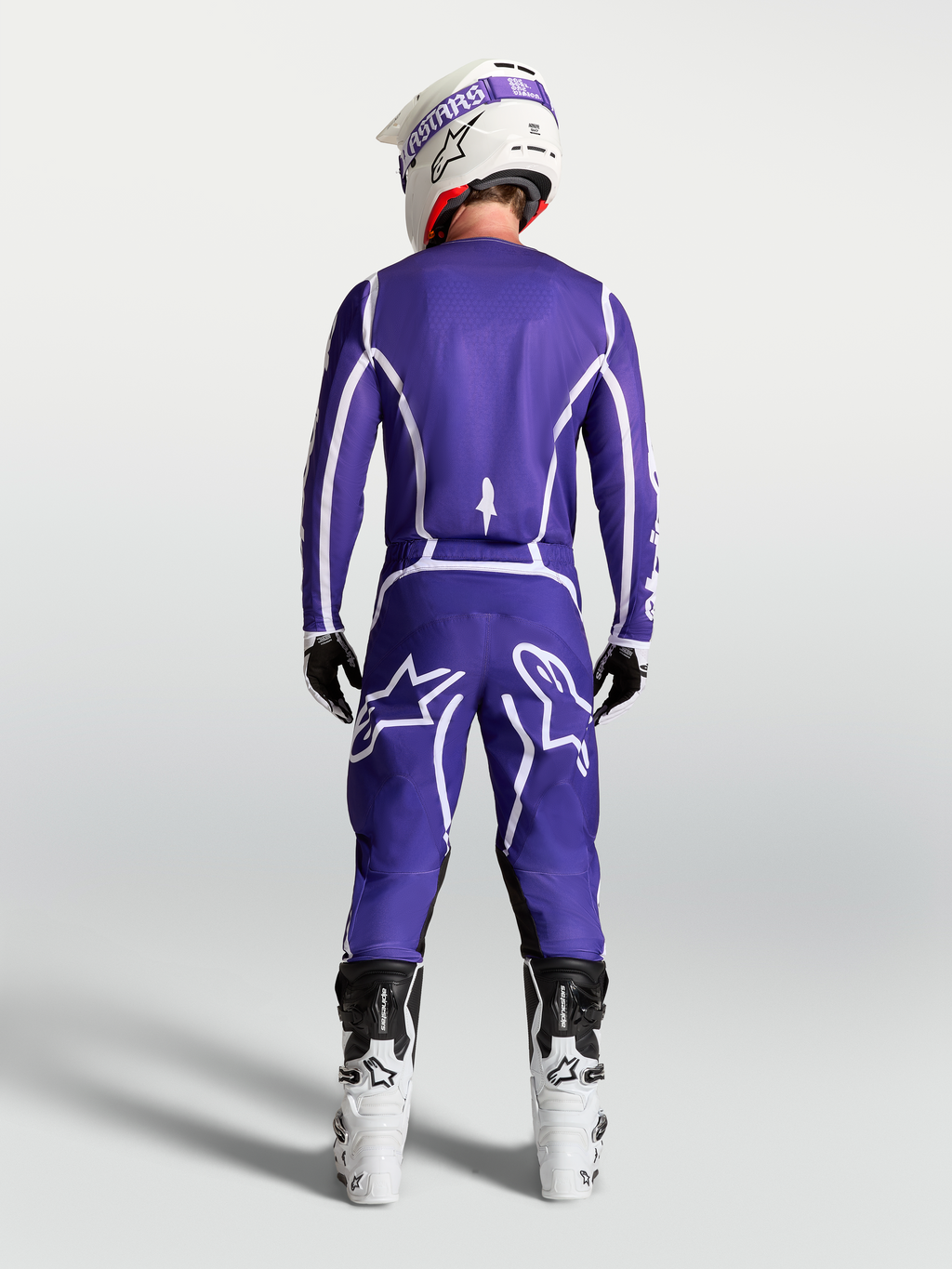Koszulka Alpinestars Fluid Apex V2, niebieska i biała, widok z tyłu na motocyklistę w komplecie motocrossowym.