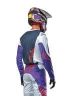 Zawodnik motocrossowy widziany od tyłu w koszulce 2024 Racer Hoen, granatowy panel tylny z jasnoszarymi ramionami i fioletowymi rękawami, jaskrawopomarańczowe logo Alpinestars, pasujące fioletowo-szare spodnie z fioletowym kaskiem motocrossowym, kompletny zestaw wyścigowy off-road