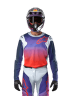 Alpinestars 2024 Racer Hoen Jersey w kolorze jasnoszarym, jaskrawym pomarańczowym i czarnym, koszulka motocrossowa noszona przez motocyklistę w kompletnym stroju, z żywym gradientem kolorów i logo gwiazdy Alpinestars na klatce piersiowej, zaprojektowana do jazdy w terenie