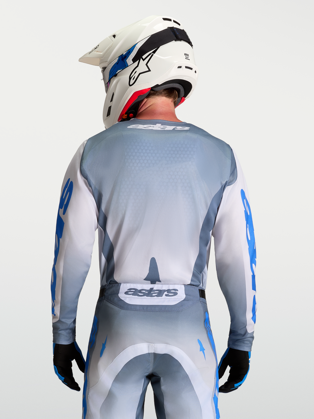 Alpinestars Racer Amber Jersey, Gray and White Motocross Jersey, Ash Gray moisture-wicking polyfabric with light lilac and UCLA blue graphics, ergonomic race fit, on-model rear view with white helmet.