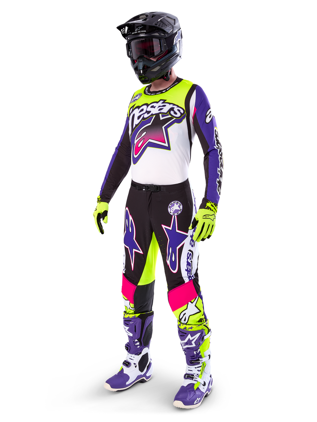 Motocyklista motocrossowy w stroju Alpinestars Limited Edition Supertech Dirt Studios®, kolorystyka biało-fioletowa i żółty fluo, czarne spodnie z wyrazistymi fioletowymi i różowymi logotypami gwiazdy, neonowożółte rękawice, fioletowo-białe buty wyścigowe, czarny kask, kompletny profesjonalny zestaw wyścigowy do jazdy terenowej