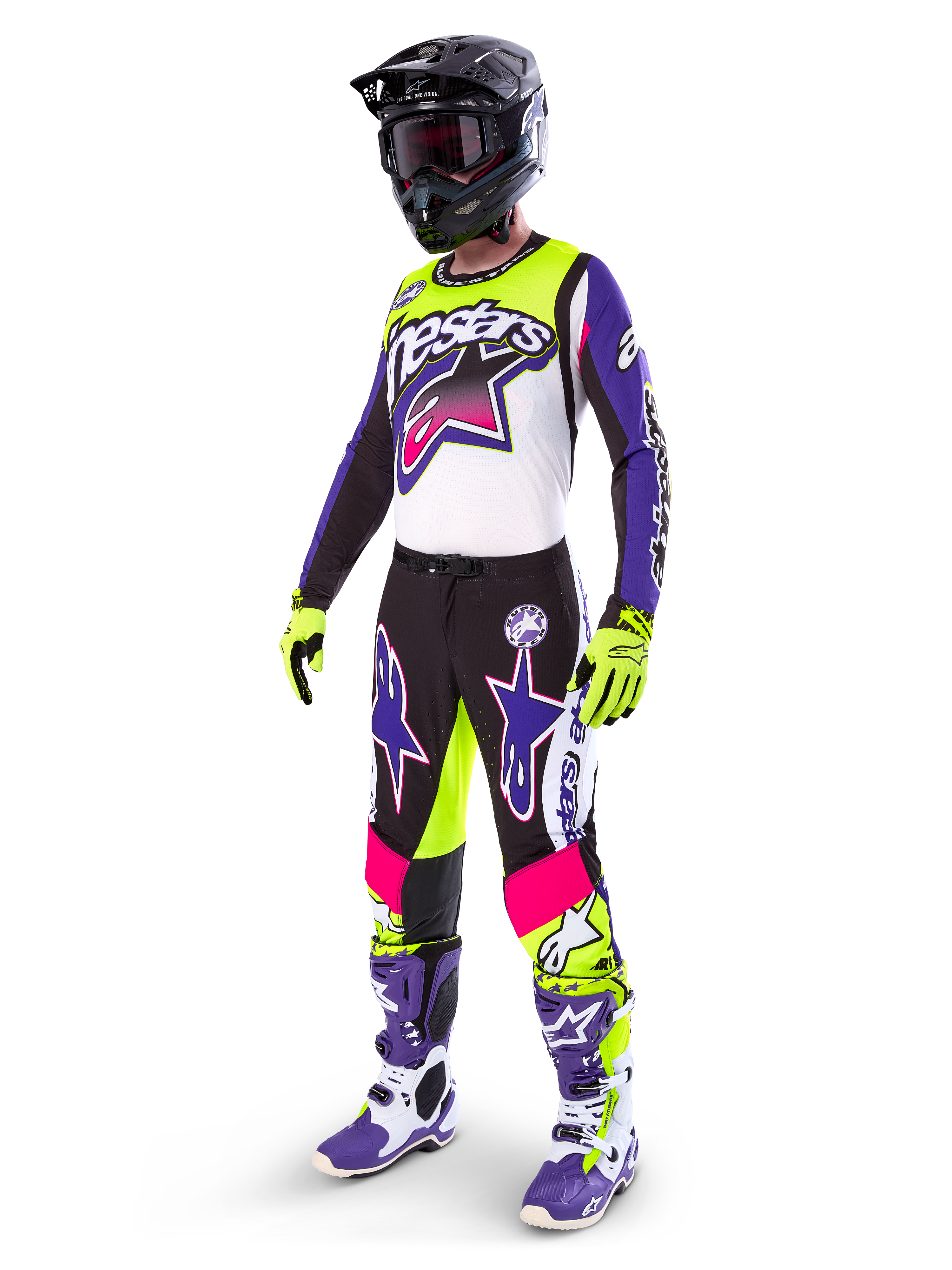 Motocyklista motocrossowy w stroju Alpinestars Limited Edition Supertech Dirt Studios®, kolorystyka biało-fioletowa i żółty fluo, czarne spodnie z wyrazistymi fioletowymi i różowymi logotypami gwiazdy, neonowożółte rękawice, fioletowo-białe buty wyścigowe, czarny kask, kompletny profesjonalny zestaw wyścigowy do jazdy terenowej