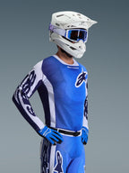 Alpinestars 2026 Racer Air Portl Jersey, koszulka motocrossowa, biało-niebieska (Ucla Blue), noszona z białym kaskiem, niebieskimi goglami i pasującymi rękawicami, przewiewna siatkowa konstrukcja do wyścigów terenowych w wysokich temperaturach
