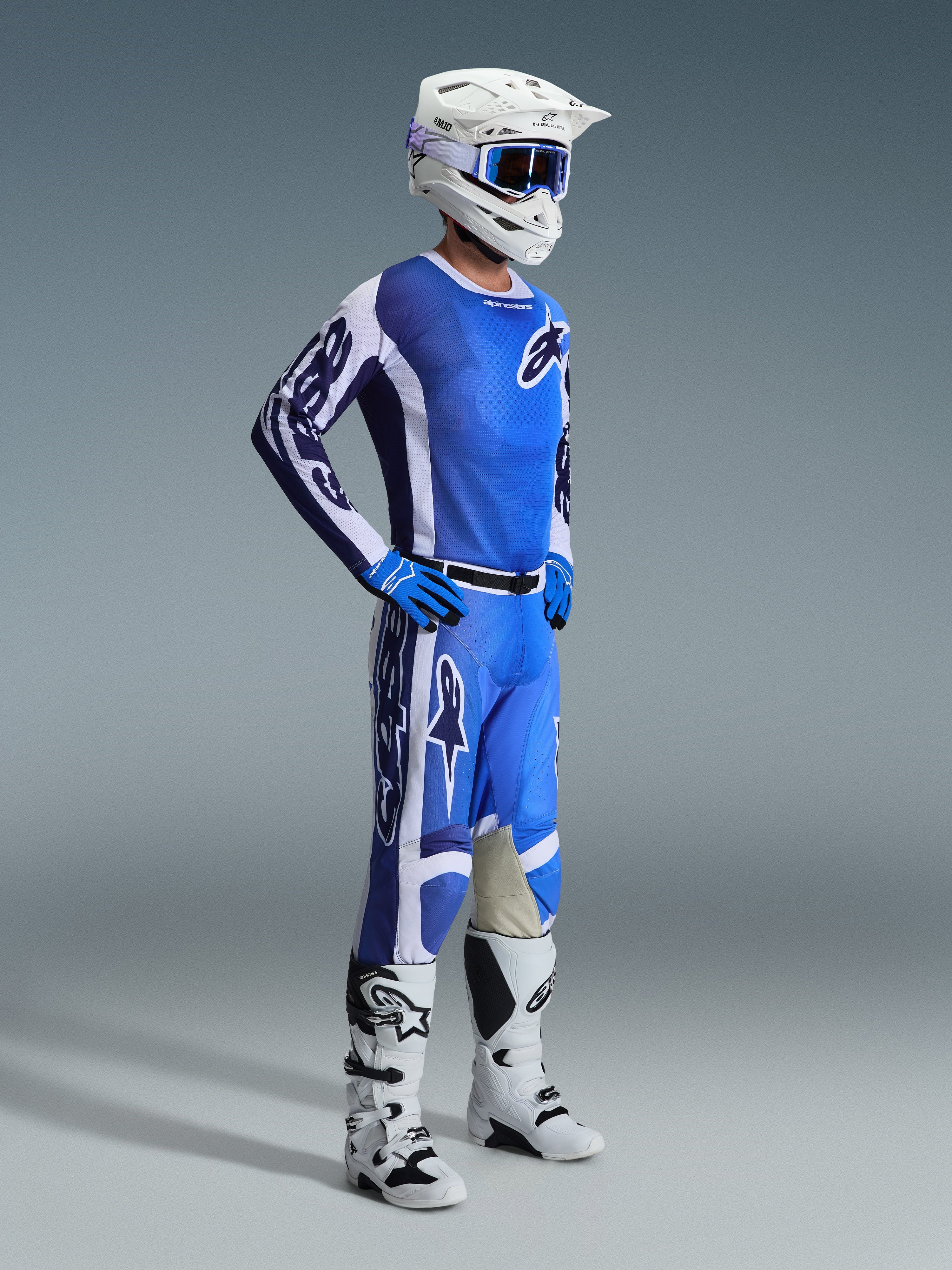 Zawodnik motocrossowy Alpinestars w koszulce 2026 Racer Air Portl w kolorze Ucla Blue i białym, dopasowane niebiesko-białe spodnie, biały kask, niebieskie gogle oraz biało-czarne buty, pełny zestaw do wyścigów off-road