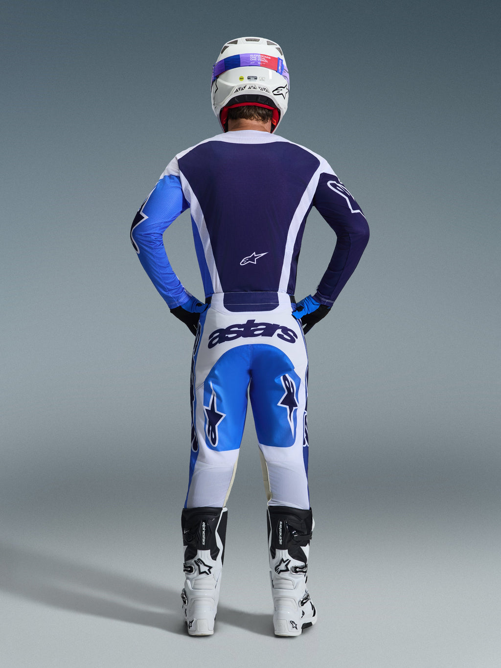 Widok od tyłu motocyklisty motocrossowego w koszulce Alpinestars 2026 Racer Air Portl w kolorze Ucla Blue White, zestawionej z pasującymi biało-niebieskimi spodniami i białymi butami, podkreślający siatkową konstrukcję na plecach zapewniającą pełny przepływ powietrza do jazdy off-road.