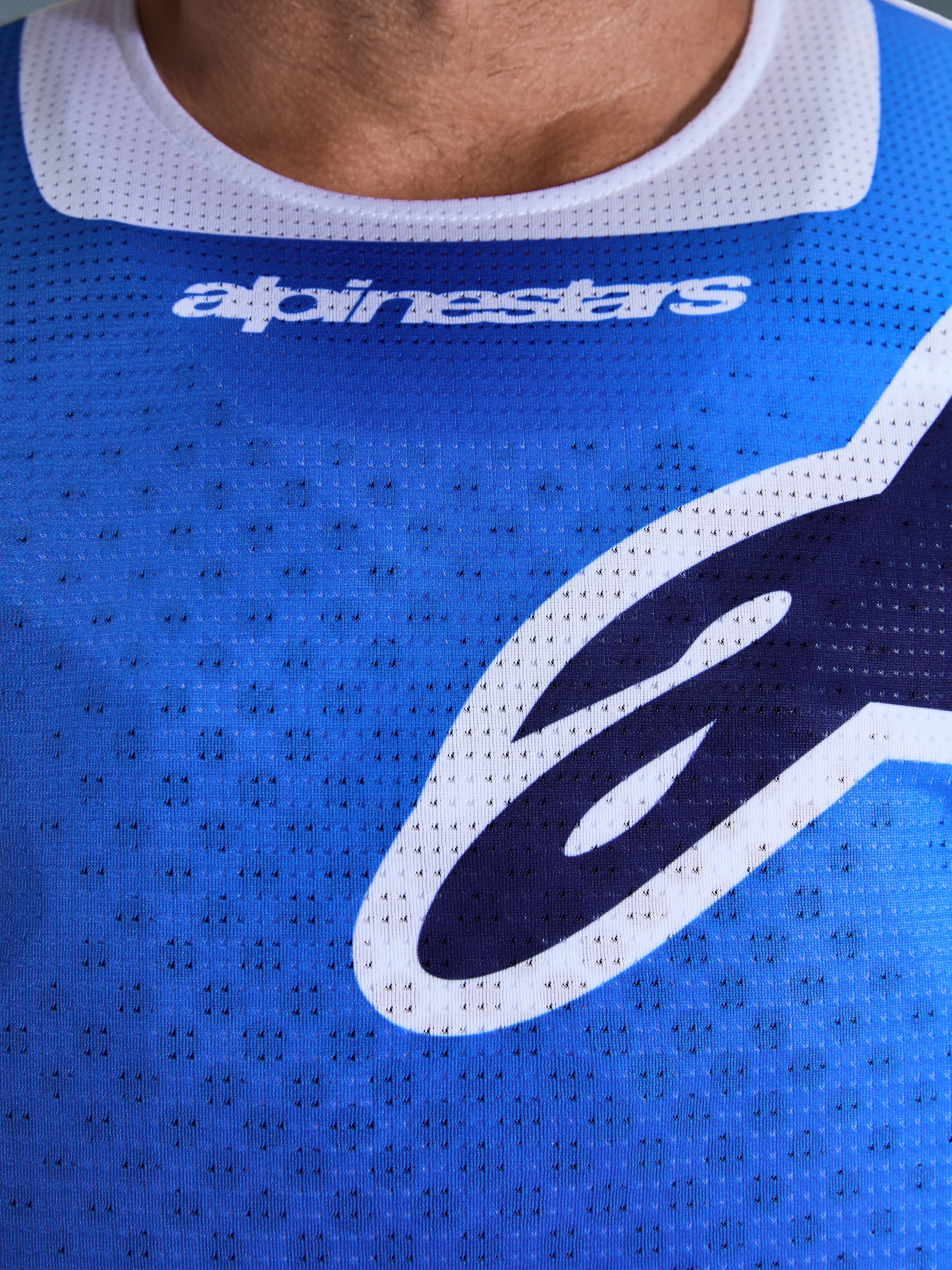 Alpinestars 2026 Racer Air Portl Jersey, koszulka motocrossowa, niebiesko-biała, zbliżenie na klatkę piersiową pokazujące oddychającą perforowaną siateczkę, białe wykończenie kołnierzyka i stylizowane logo Alpinestars