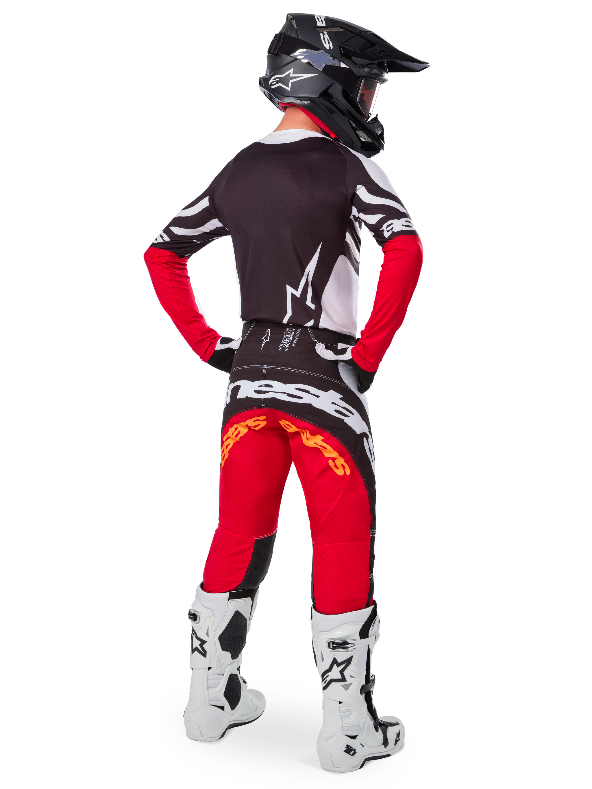 Zawodnik motocrossowy widok z tyłu w koszulce Alpinestars Limited Edition Techstar Deep Jersey w kolorze Black White High Red, czarny tył z białym logo gwiazdy i czerwone rękawy, w zestawieniu z dopasowanymi czerwono-czarnymi spodniami, biało-czarnymi butami i czarnym kaskiem, kompletny strój do wyścigów terenowych.