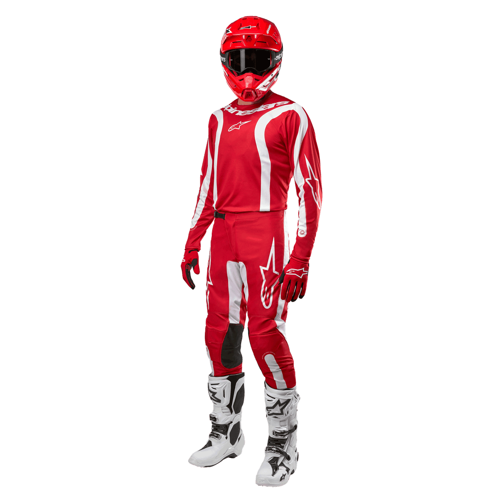 Zawodnik motocrossowy w pełnym stroju wyścigowym, koszulka Alpinestars 2024 Fluid Lurv w kolorze Mars Red i białym, dopasowane czerwone spodnie z białymi akcentami, czerwony kask, czerwone rękawice oraz biało-czarne buty, skoordynowany zestaw do wyścigów off-road