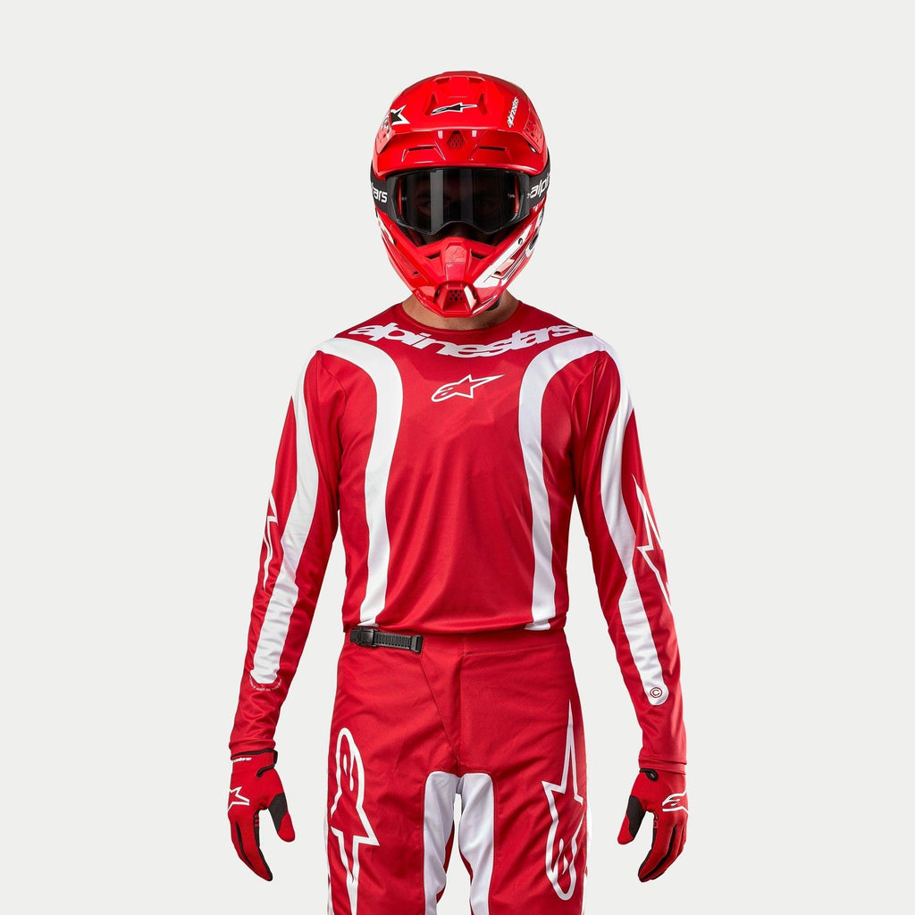 Alpinestars 2024 Fluid Lurv Jersey, koszulka motocrossowa, czerwono-biała, noszona z dopasowanymi czerwonymi spodniami, kaskiem i rękawicami, białe akcenty graficzne na rękawach, wyraziste logo na klatce piersiowej, sportowy krój do wyścigów terenowych