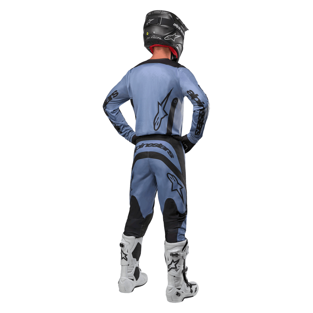 Zawodnik motocrossowy widziany od tyłu w koszulce Alpinestars 2024 Fluid Lurv i pasujących spodniach w kolorze jasnoniebiesko-czarnym, z czarnymi logotypami na plecach i rękawach, czarny kask i białe buty