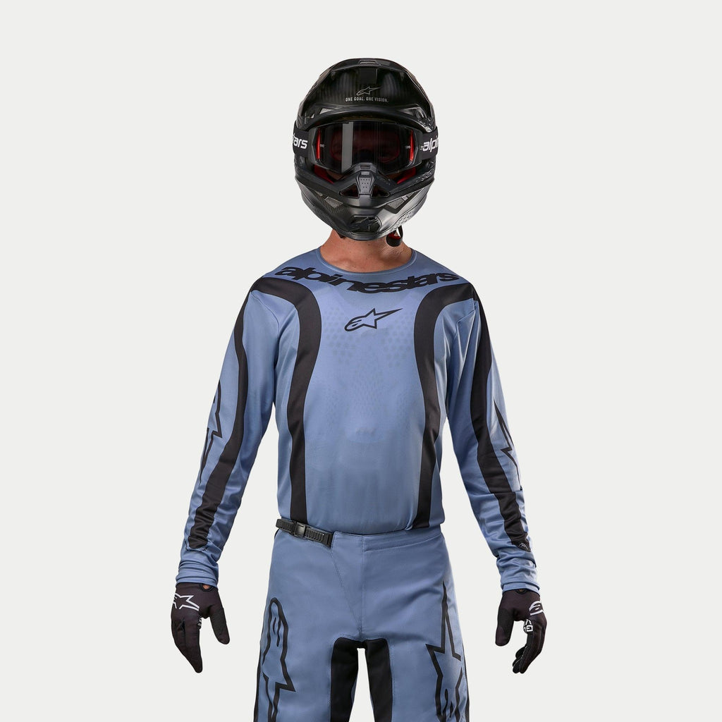 Alpinestars 2024 Fluid Lurv Jersey, koszulka motocrossowa, jasnoniebieska i czarna, noszona przez motocyklistę z dopasowanymi spodniami, czarny kask z czerwonymi goglami i czarne rękawice, skoordynowany strój do wyścigów terenowych