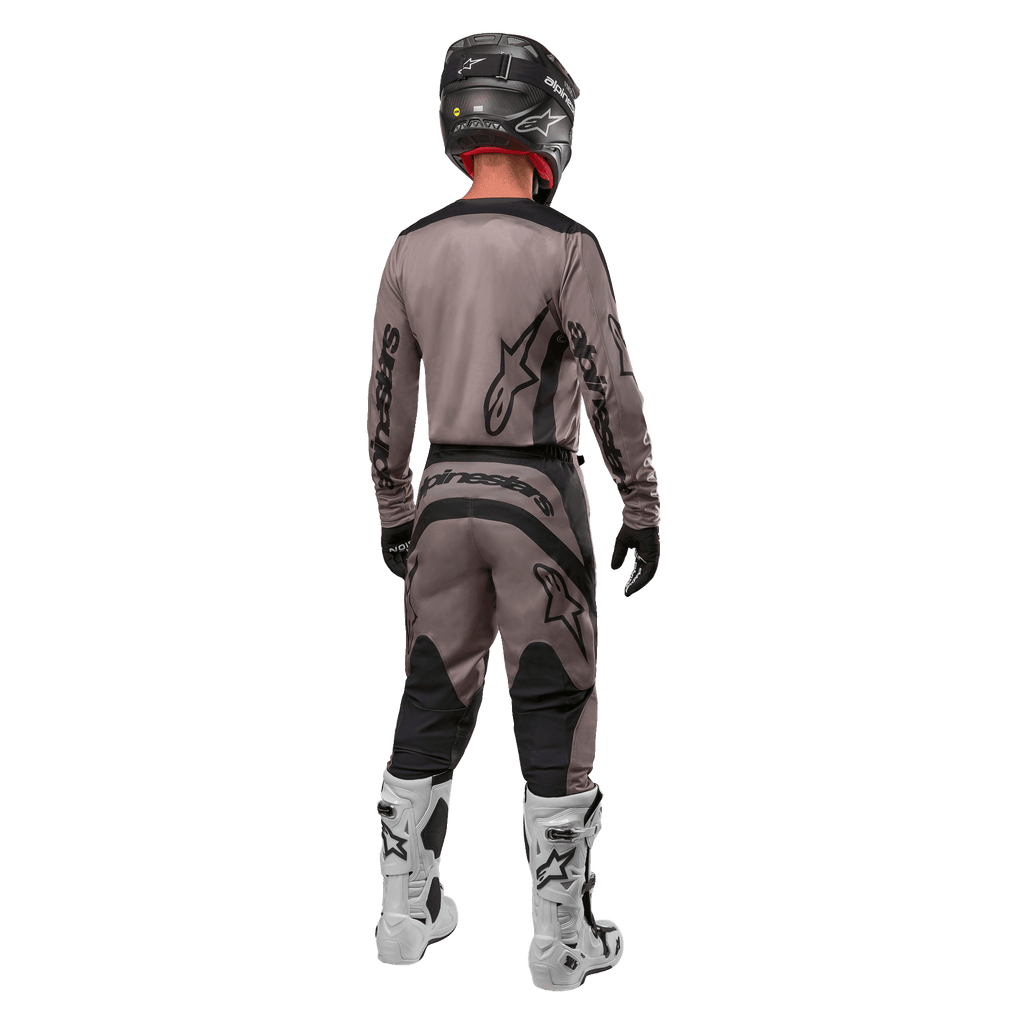 Alpinestars 2024 Fluid Lurv Jersey, koszulka motocrossowa, Mud Black, widok z tyłu zawodnika motocrossowego w dopasowanym stroju wyścigowym, czarny kask i białe buty, wyraźne czarne logotypy Alpinestars, sportowy krój zapewniający wydajność w terenie