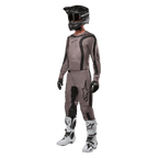 Zawodnik motocrossowy ubrany w pełny strój wyścigowy z koszulką Alpinestars 2024 Fluid Lurv w kolorze Mud Black, w zestawieniu z dopasowanymi spodniami, czarnym kaskiem z goglami, biało-czarnymi butami i czarnymi rękawicami, skoordynowany zestaw do wyścigów terenowych