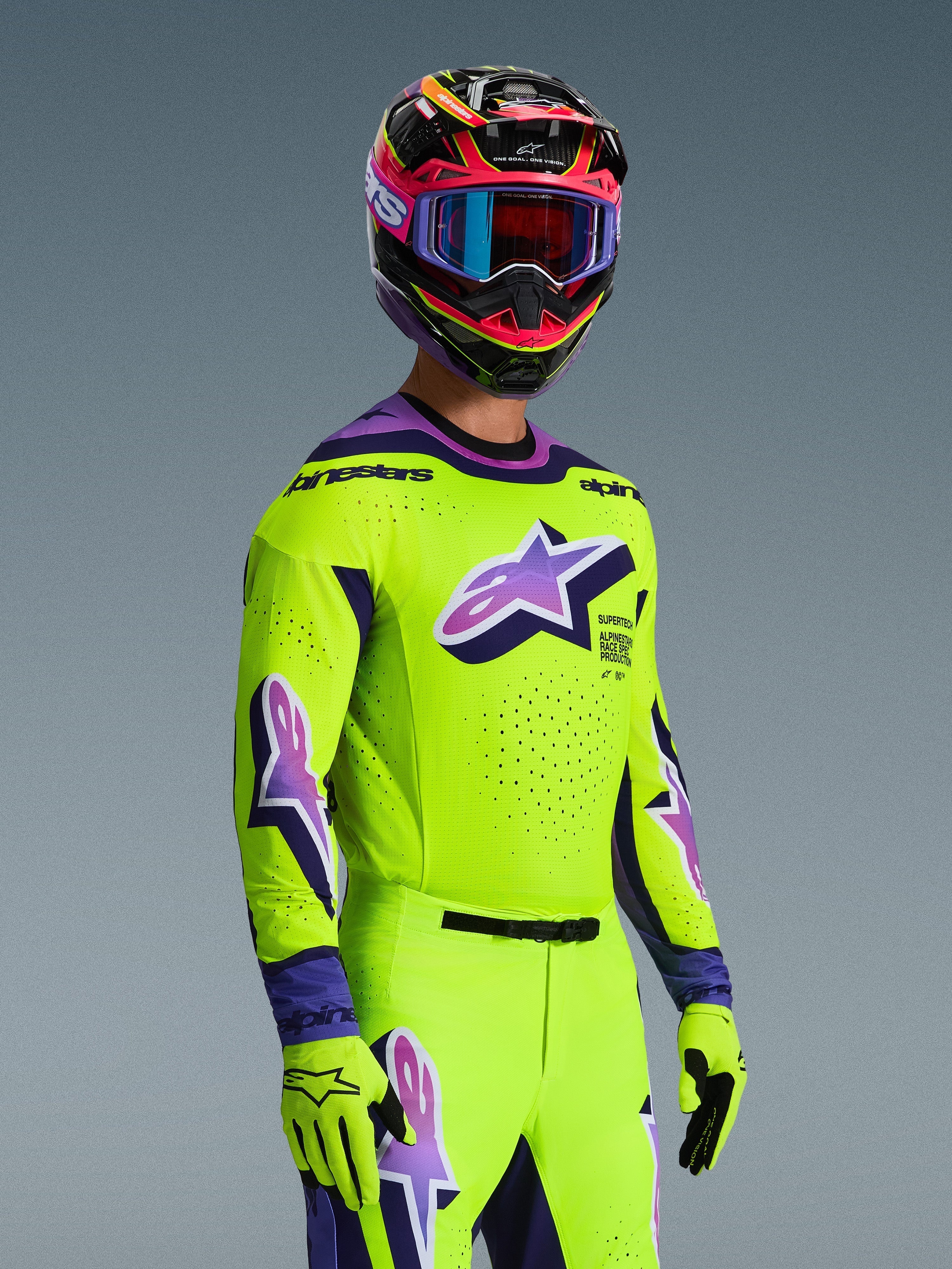 Zawodnik motocrossowy w koszulce Alpinestars 2026 Supertech Vista, jaskrawożółta z fioletowymi i czarnymi akcentami, pasujące żółte spodnie i rękawice, wielokolorowy kask z fioletowymi goglami, laserowo wycinane perforacje i duże logo Astar na piersi, profesjonalny strój wyścigowy