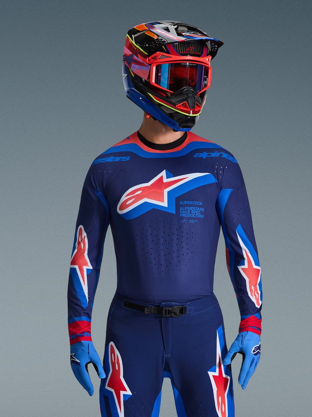 Alpinestars 2026 Supertech Vista Gear Set, profesjonalna odzież motocrossowa, granatowa bluza i spodnie z wyrazistymi czerwono-białymi logotypami gwiazdy, w połączeniu z wielokolorowym kaskiem wyścigowym, czerwonymi goglami i jasnoniebieskimi rękawicami, profesjonalny zestaw wyścigowy