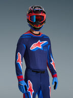Zawodnik motocrossowy w koszulce 2026 Supertech Vista w kolorach ciemnogranatowym, koralowym i kobaltowym, pasujące spodnie i rękawice, wielokolorowy kask z czerwonymi goglami, profesjonalny zestaw odzieży do wyścigów terenowych