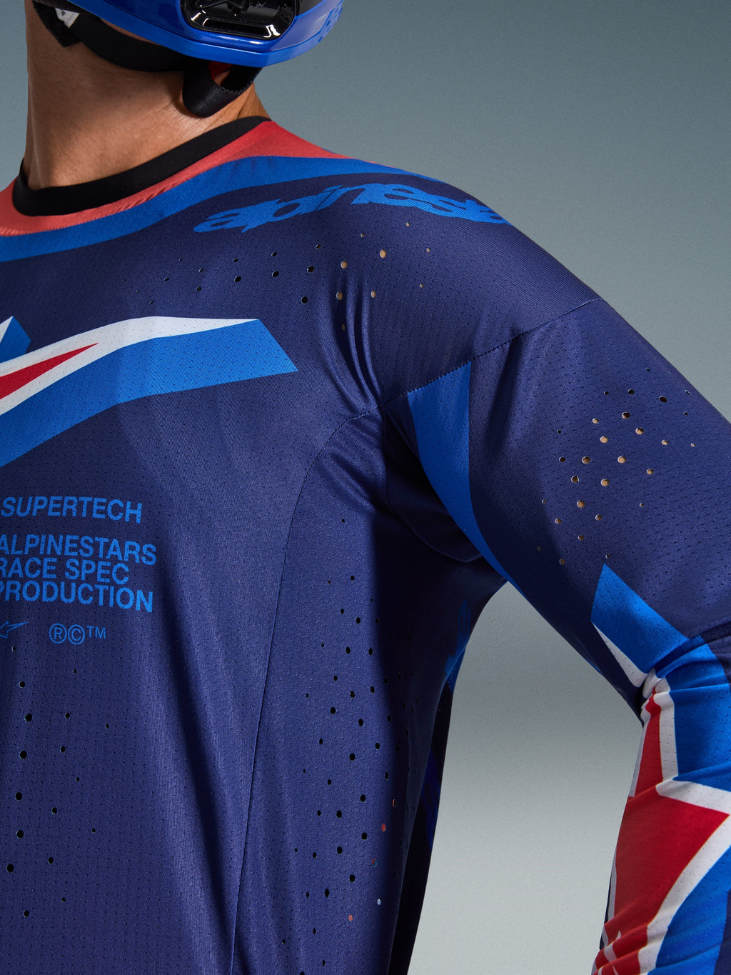 Alpinestars 2026 Supertech Vista Jersey, zbliżenie na ciemnogranatową i kobaltową koszulkę z kołnierzykiem Hot Coral, laserowo wycinane otwory wentylacyjne i branding Alpinestars Race Spec, sportowa siateczkowa konstrukcja do wyścigów motocrossowych