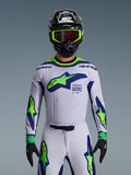 Alpinestars 2026 Supertech Vista Jersey, koszulka motocrossowa, jasnoszara, żółta fluo i niebieska, noszona przez zawodnika z pasującymi spodniami i czarnym kaskiem, duże logo na klatce piersiowej, laserowo wycinane perforacje wentylacyjne, sportowy krój pro-level