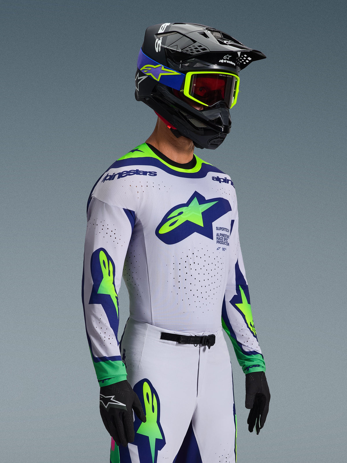 Zawodnik motocrossowy w koszulce 2026 Supertech Vista w kolorze jasnoszarym z żółtymi fluorescencyjnymi i niebieskimi akcentami, z dużymi logo gwiazdy na klatce piersiowej i rękawach, pasujące spodnie i kask z goglami fluo, czarne rękawice, profesjonalny sprzęt motocrossowy