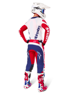 Zawodnik motocrossowy widziany od tyłu w zestawie Alpinestars Limited Edition Techstar Fortitude, kolorystyka Bright Red White and Blue, białe logo Alpinestars na czerwonych rękawach i granatowe logo na białych plecach, biały kask motocrossowy i pasujące buty wyścigowe.