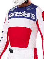 Alpinestars Limited Edition Techstar Fortitude Gear Set, koszulka i spodnie motocrossowe w barwach czerwono-biało-niebieskich, biała koszulka z granatowym górnym panelem i dużą czerwoną grafiką na środku, pasujące biało-czerwone spodnie z klamrą magnetyczną SX2, sportowy krój z laserowo wycinanymi perforacjami do wyścigów off-road