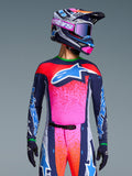 Zawodnik motocrossowy w koszulce Alpinestars Limited Edition Supertech Records, wyrazisty różowo-granatowy design z pomarańczowymi nakrapianymi wzorami i jasnoniebieskim logo z gwiazdą, pasujący kask i gogle, profesjonalna odzież wyścigowa