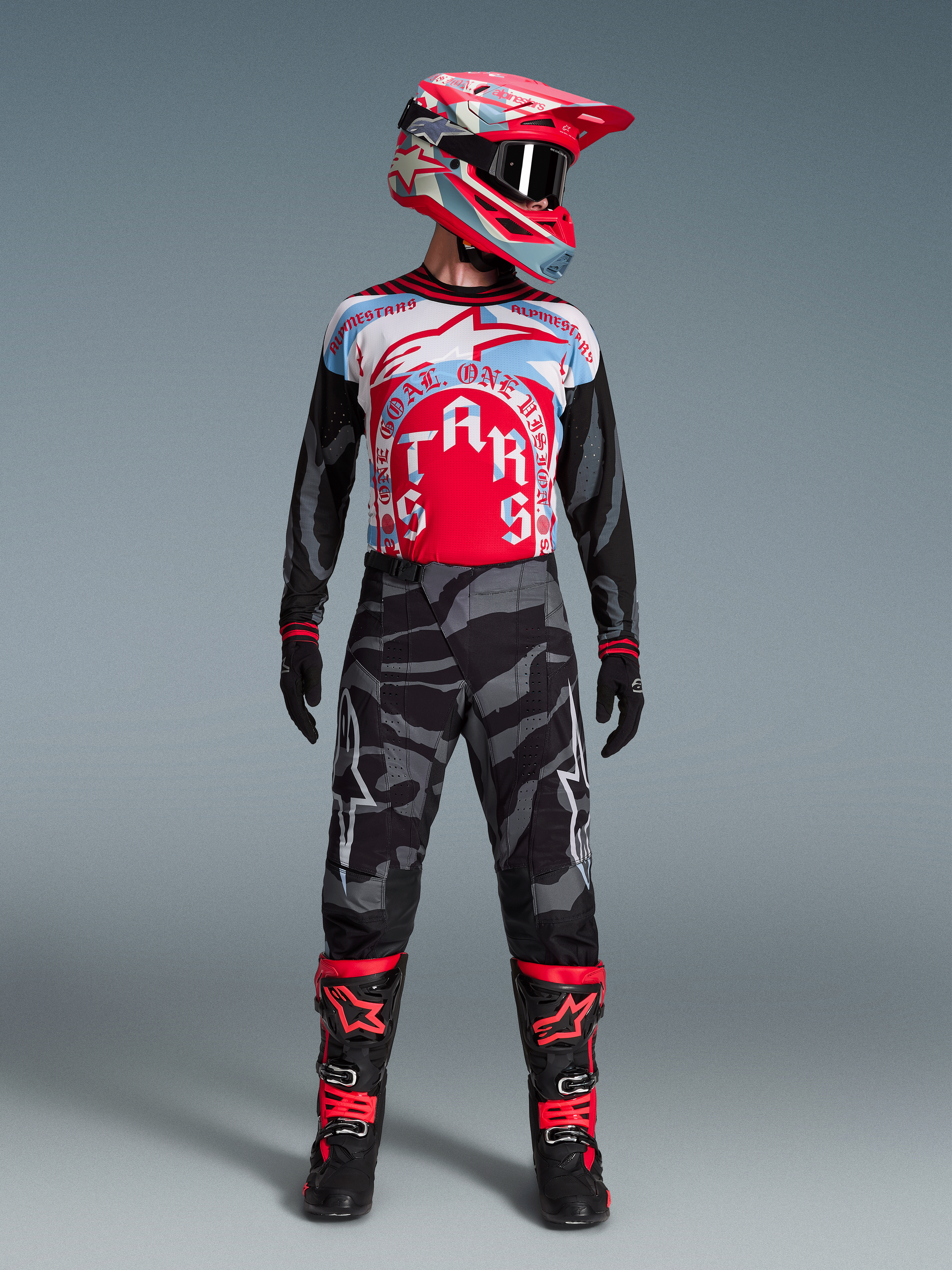 Zestaw Alpinestars Techstar Beast Coast, czerwono-niebieska koszulka MX, spodnie camo, czerwony kask i buty motocyklowe.
