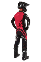 Zawodnik motocrossowy widziany od tyłu w koszulce 2024 Supertech Ward w kolorze Black Red Berry, z jaskrawoczerwonym panelem tylnym i czarnymi rękawami z białym brandingiem Alpinestars. W zestawie z dopasowanymi spodniami motocrossowymi, czarnymi butami Tech 10 i czarnym kaskiem z włókna węglowego, tworzącymi profesjonalny komplet wyścigowy.