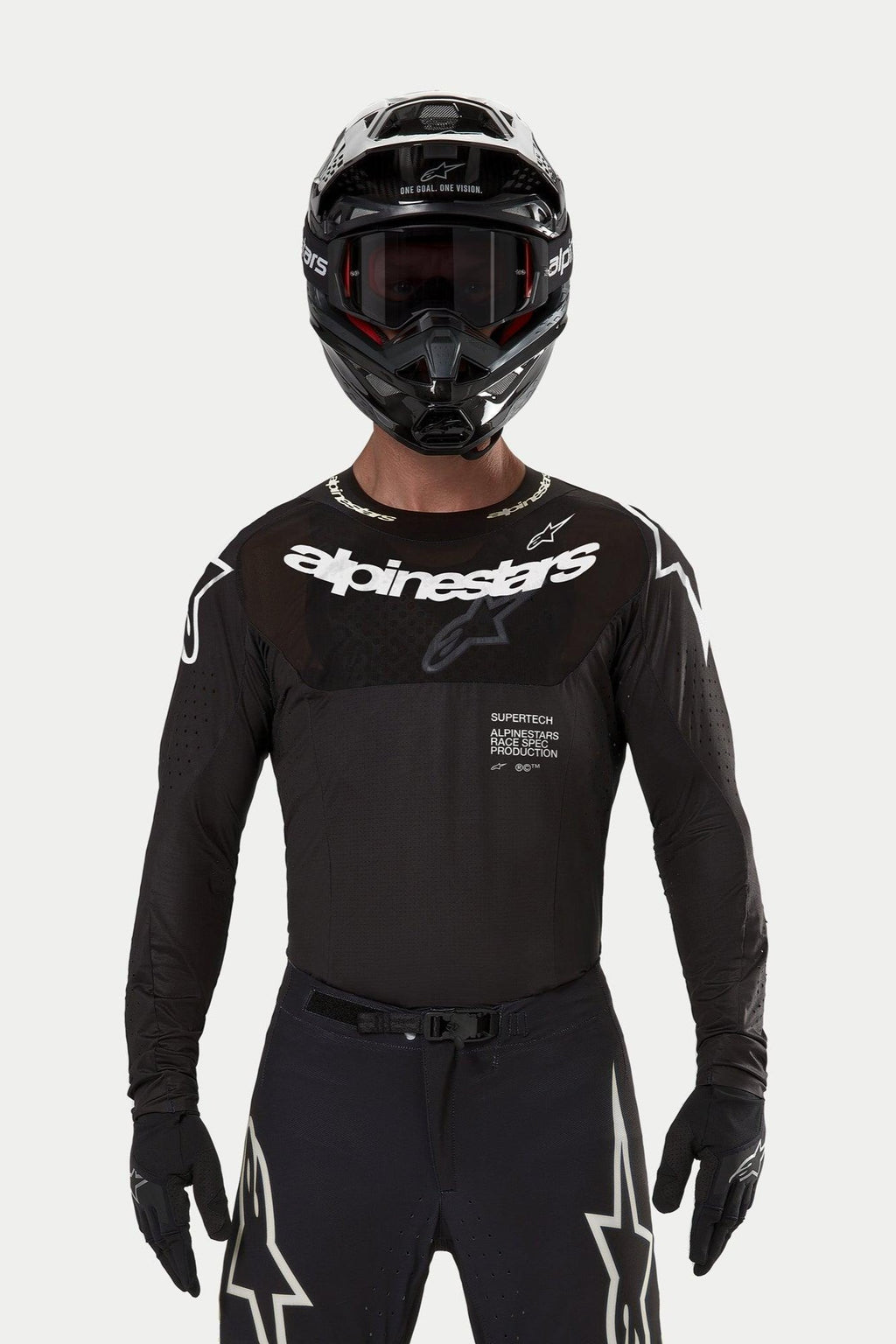 Motocyklista motocrossowy w koszulce Alpinestars Supertech Ward 2024 w kolorze czarnym, sportowy krój wyścigowy, białe logo Alpinestars na klatce piersiowej, laserowo wycinane perforacje i napis „Supertech Race Spec”, w czarnym kasku i goglach do wyścigów off-road