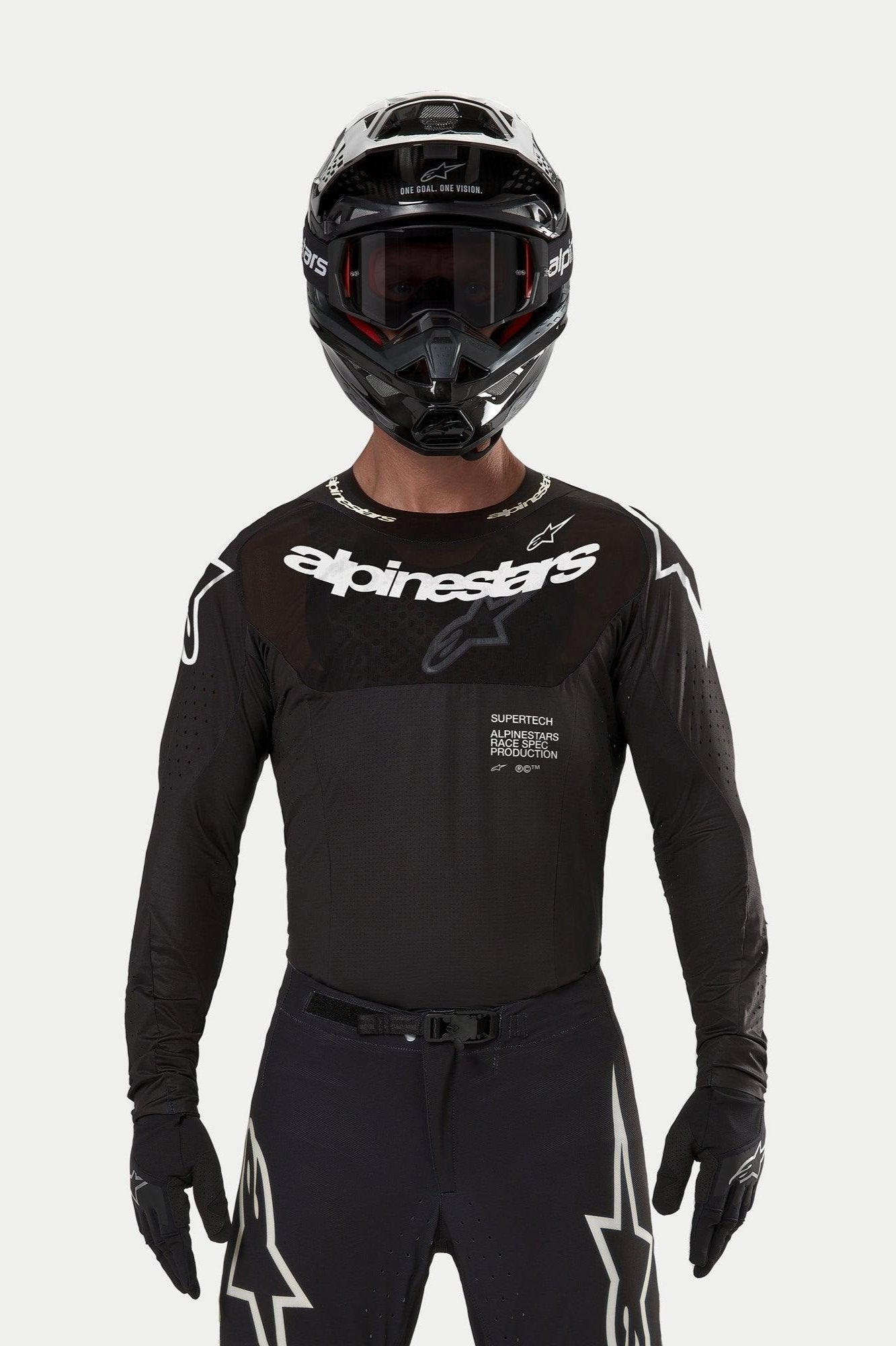 Motocyklista motocrossowy w koszulce Alpinestars Supertech Ward 2024 w kolorze czarnym, sportowy krój wyścigowy, białe logo Alpinestars na klatce piersiowej, laserowo wycinane perforacje i napis „Supertech Race Spec”, w czarnym kasku i goglach do wyścigów off-road