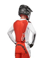 Kierowca motocrossowy w koszulce 2024 Supertech Ward Jersey w kolorze White Hot Orange, widok z tyłu ukazujący pomarańczowy panel tylny i białe rękawy z czarnym brandingiem Alpinestars, w zestawie z dopasowanymi spodniami i czarnym kaskiem, profesjonalny sprzęt do wyścigów terenowych